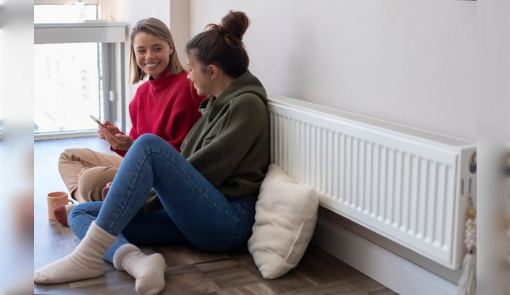 Due giovani donne siedono davanti al termosifone